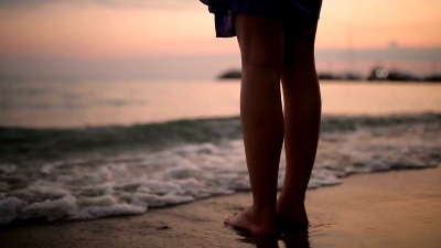 日落时分，年轻女子在沙滩上的海浪中漫步