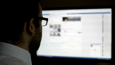一个在社交网络上使用的人。商人看新闻。计算机显示器显示模糊Facebook新闻馈送页面年轻女孩在线。