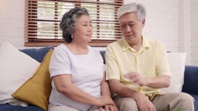 亚洲老年夫妇手牵手一起在客厅，夫妻俩感觉快乐分享和支持对方躺在家里的沙发上。生活方式在家中的高级家庭概念。