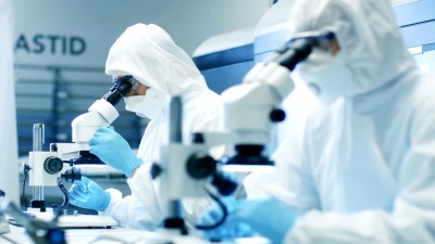 两名穿着无菌洁净服的工程师/科学家/技术人员使用显微镜进行组件调整和研究。他们在一家电子元件制造厂工作。
