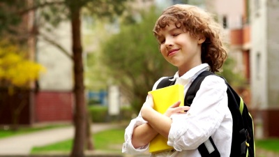 一名小学生手里拿着一本书的特写肖像。男孩若有所思地望着远方，带着梦幻般的微笑。卷发白色衬衫。回学校