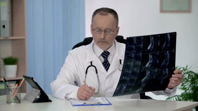 脊柱外科医生检查脊椎MRI，在患者的医疗卡上做笔记