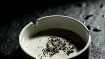 将点燃的香烟和吸烟的香烟放在烟灰缸里，旁边放一杯威士忌的镜头