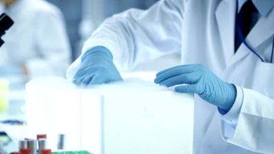 一位医学研究科学家打开冷藏箱的特写镜头，取出带有样品的培养皿并检查它。他在一个繁忙的现代实验中心工作。