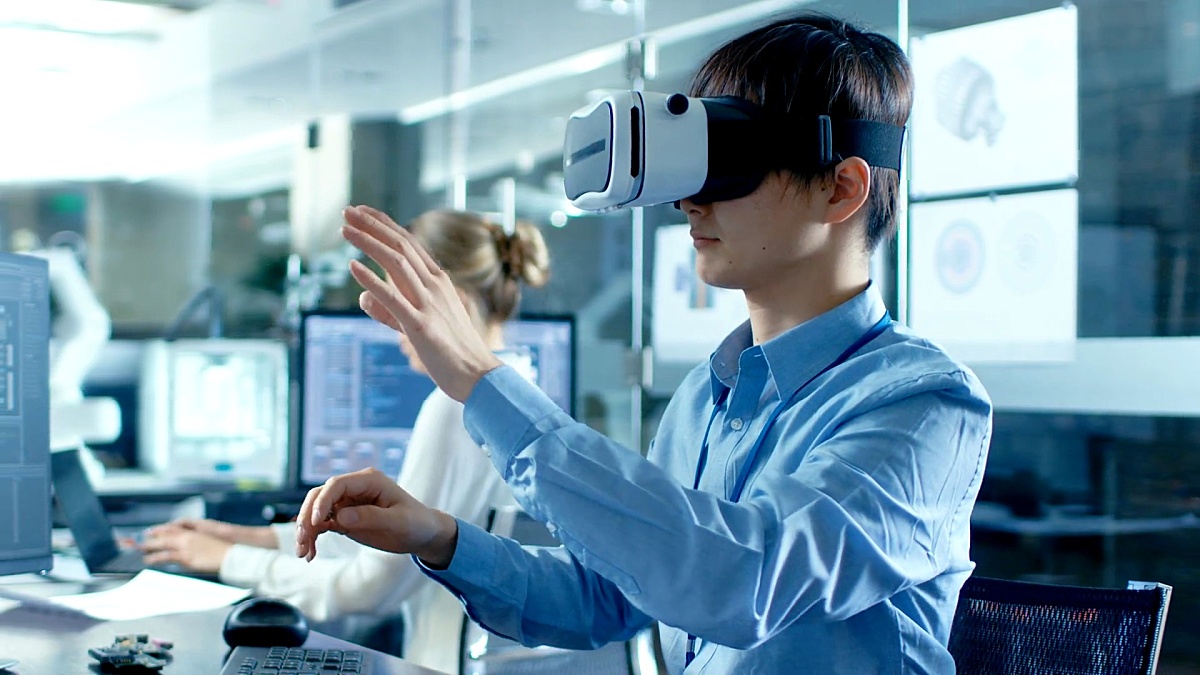 计算机科学工程师戴着虚拟现实头盔与3D建模一起工作，做手势。在后台工程局与忙碌的同事。