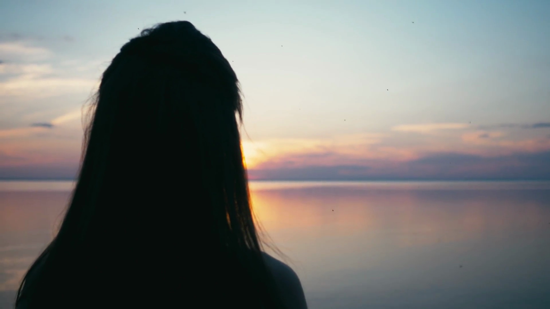 美丽的女人在夕阳下用手做心形女孩举起爱的象征手势橙色的太阳耀斑