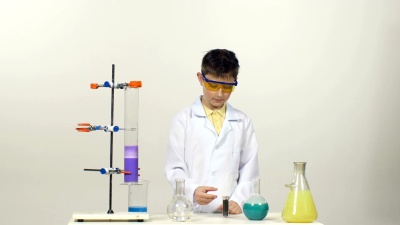 穿着制服，戴着防护眼镜的小男孩化学家成功地在白色背景上测试了新配方和奇迹