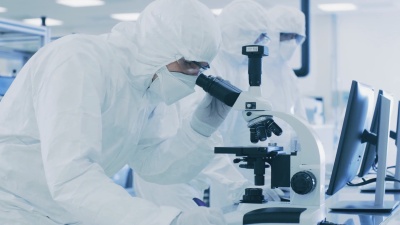在实验室里，穿着防护服的科学家们在做研究，使用显微镜并将数据输入个人电脑。生产半导体和医药用品的现代制造厂。