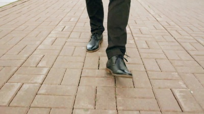 Steadicam特写镜头穿着鞋子走在街上人行道前的商人