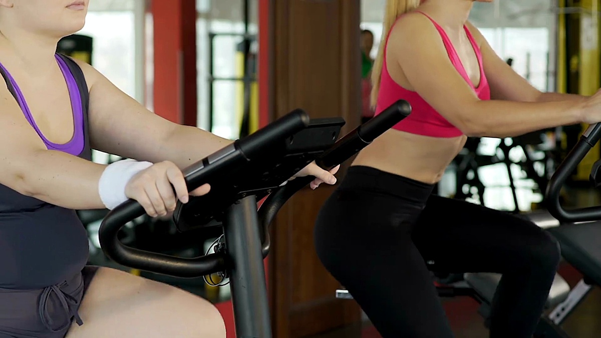 健身房身材曲线健美的哈代女孩，将脂肪驱逐在健身自行车上