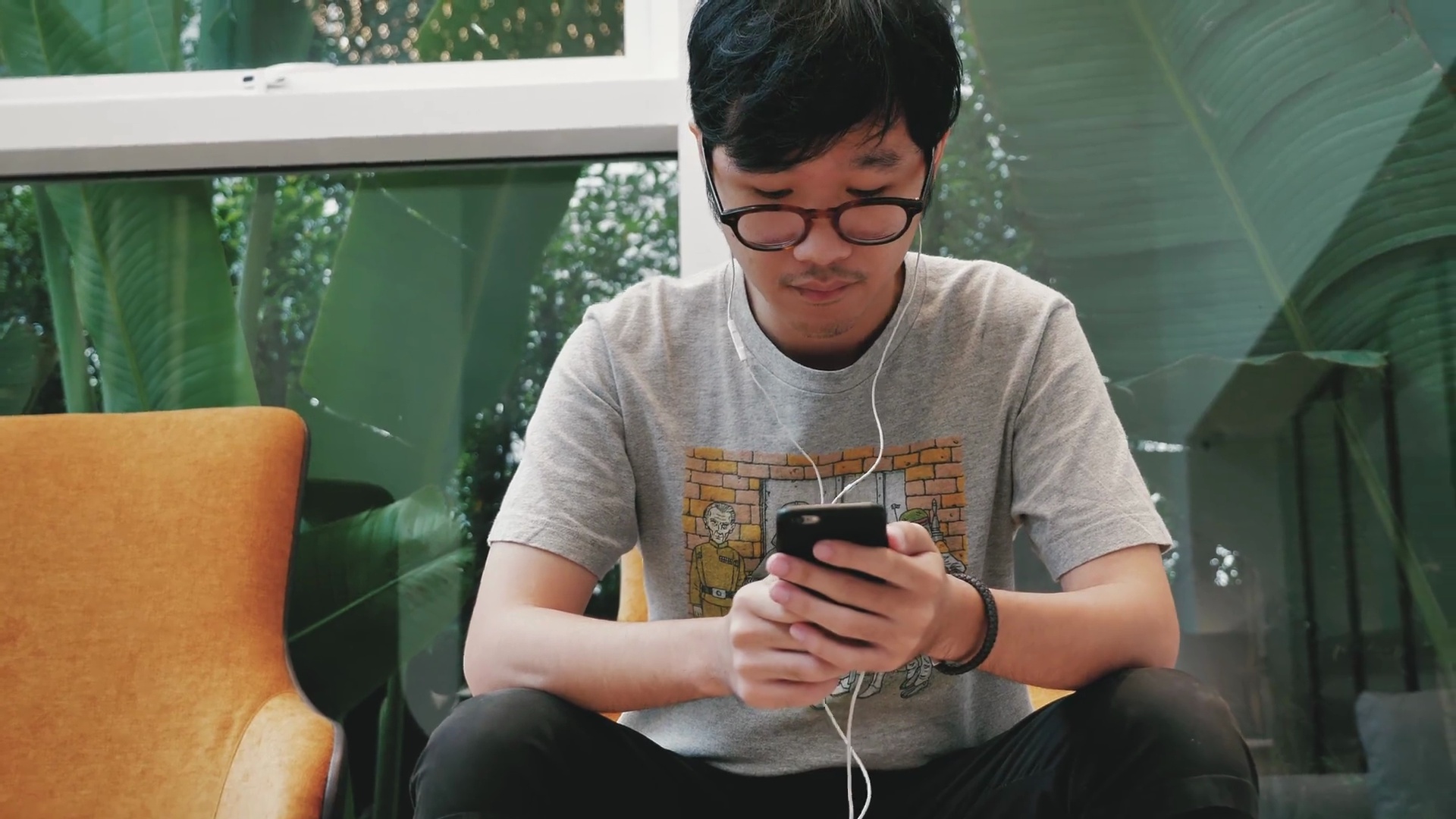 亚洲十几岁的男孩在手机上戴着耳机听音乐。