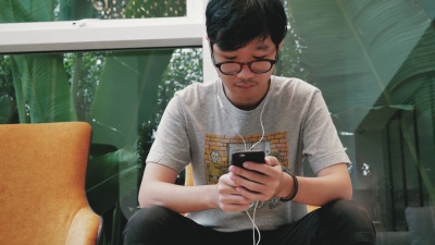 亚洲十几岁的男孩在手机上戴着耳机听音乐。