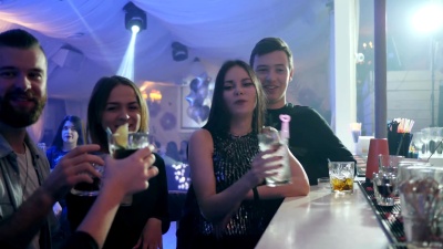 喝着五颜六色的鸡尾酒的男女举杯，在夜总会的吧台附近玩得很开心