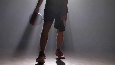 近距离拍摄在有泛光灯的薄雾房间里男人的双腿运球