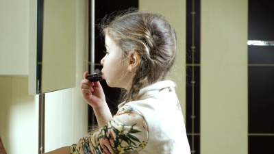 可爱的小女孩在浴室的镜子前用口红涂嘴唇