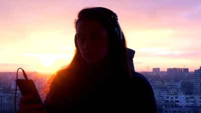 日落时分在城市的电话上跳舞和听音乐的女人的剪影