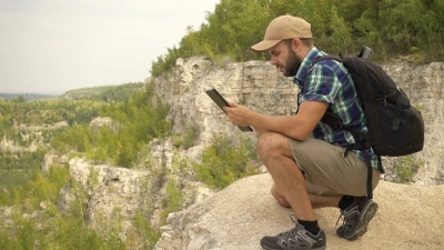 旅游者他坐在山上，用平板电脑。在树林里背着背包的男人。徒步旅行。森林之旅。露营。闲暇。生态旅游。狂野。冒险开始了。慢动作。
