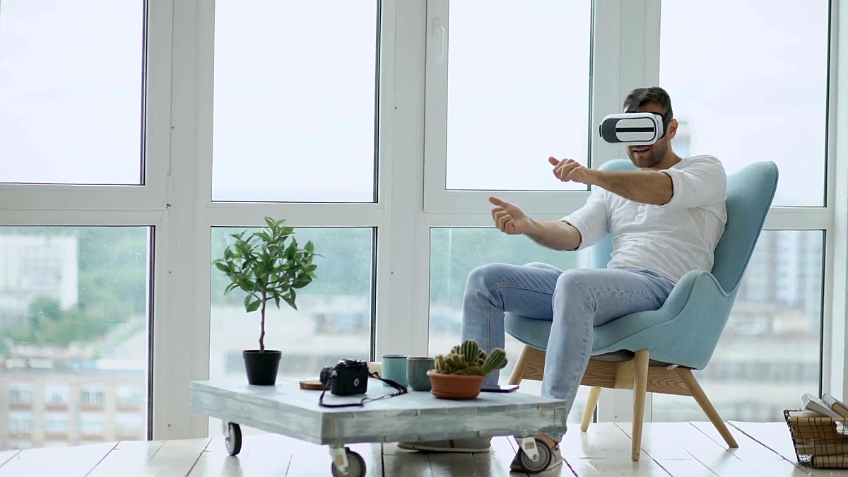 年轻人有使用虚拟现实头盔坐在阳台上的椅子上玩电脑赛车游戏的VR体验
