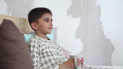 小男孩坐在床上用杯子喝茶