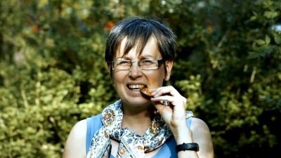 测试硬币，银比特币。40多岁的高加索女人在户外的绿灌木树叶背景下咬比特币，做着不开心的表情。