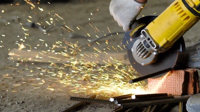近距离拍摄建筑工人的双手，人们拿着锯片用金属工作，一名男子在建筑工地上切下一块金属棒