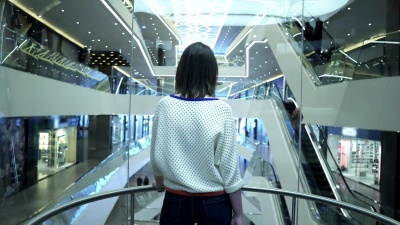 一名妇女爬上购物中心的电梯，从后面观看