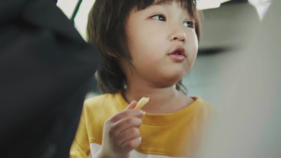 泰国小男孩在乘坐出租车旅行时拿着并吃着炸薯条，他的妈妈在他旁边-股票视频
