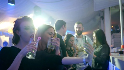 年轻的朋友女人手中拿着鸡尾酒，在灯光的背景下在夜总会的吧台后面自拍