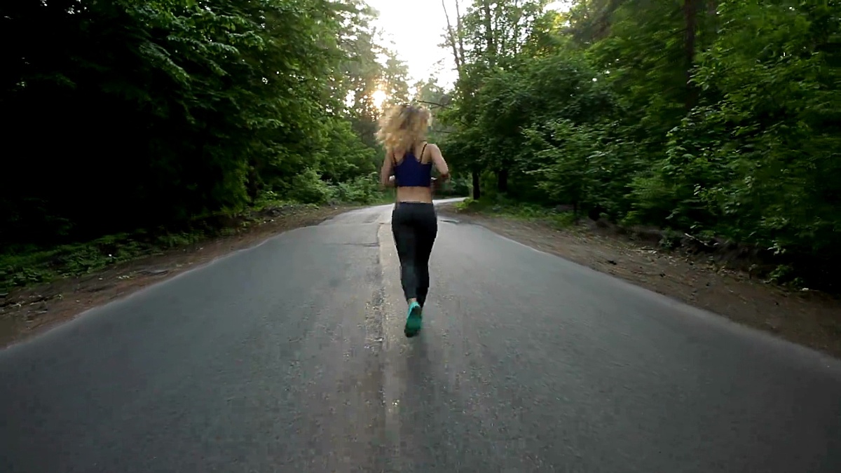 健美的女孩在森林中的公路上奔跑。户外健身。用Sticicam拍摄