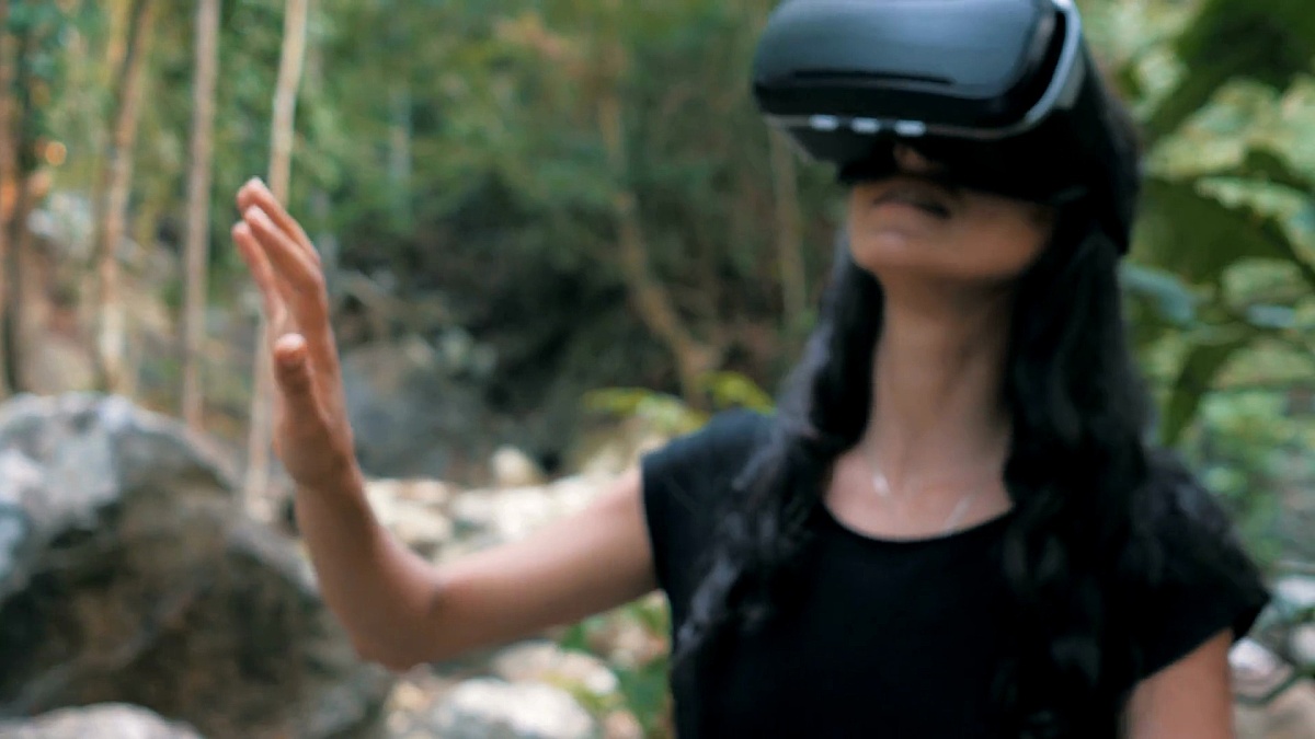 美丽的年轻黑发女子在丛林中使用虚拟现实眼镜