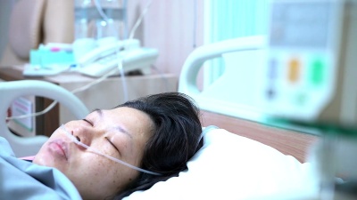 卧床不起的女性患者躺在医院病床上，在手术后恢复的同时接受输液。