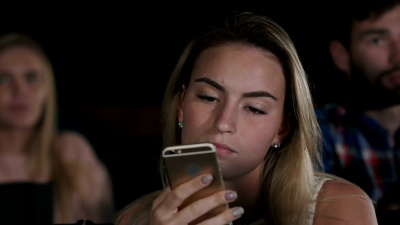 一位美丽的年轻女性在当地电影院看电影时发短信的镜头