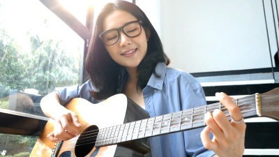 迷人的亚洲女子在家中微笑着弹吉他。