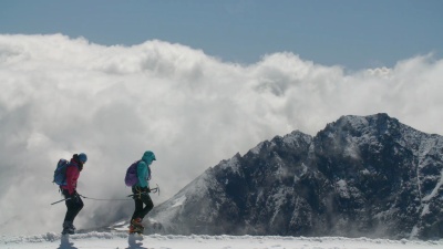两名登山者穿越冰川和山脊，远处有暴风云。