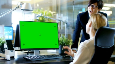 在办公室女商人坐在办公桌前与她的经理交谈时，她的个人电脑显示了模拟绿屏。专业商务人士在时尚的办公室。