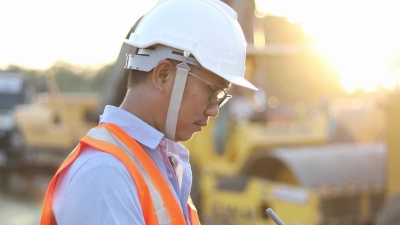 亚洲工程师带着安全帽在施工现场使用平板电脑进行检查和工作