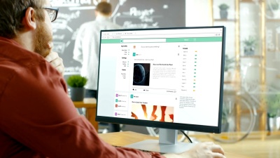 有创意的办公室工作人员浏览社交网络页面，他在个人电脑上滚动他的墙。在背景时尚的创意工作室与黑板墙。