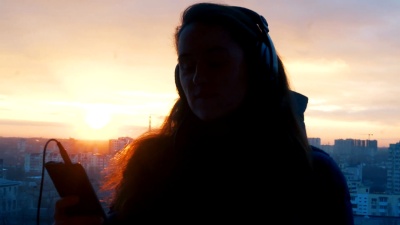日落时分在城市的电话上跳舞和听音乐的女人的剪影
