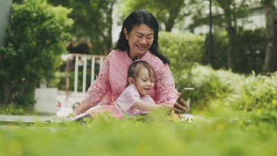由祖母和她的侄女组成的东南亚家庭正在花园里用智能手机放松
