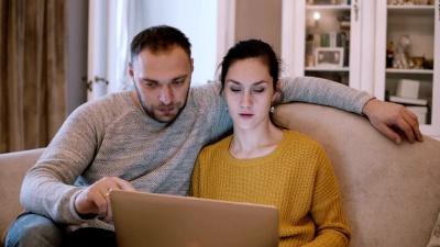 坐在沙发上拿着电脑的年轻夫妇。男人和女人坐在起居室里使用笔记本电脑