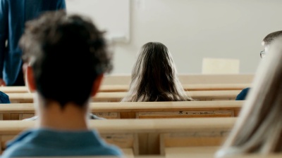 学生们在演讲厅后视，听一位教授讲课，一位学生举手提问。