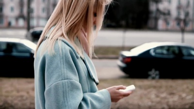 慢动作的金发碧眼的女人穿着蓝色外套发短信。侧视图。女孩在旅途中发送信息。生活方式。快节奏的生活