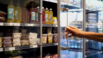 在食品市场购物的一位面目全非的高级女士从冰箱里拿出一种产品放在购物车里
