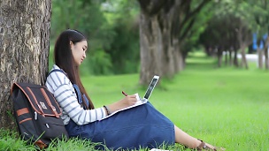 微笑美丽的亚洲女孩看书夏天在公园的树上工作放松时间