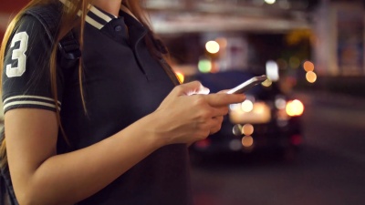 女性在夜间从智能手机上请求并等待Uber