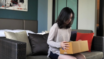 年轻女子坐在家里的沙发上打开纸板箱