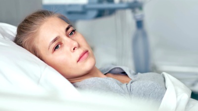 年轻的女病人躺在病房里。悲伤和不安的女人思考现代诊所的生活
