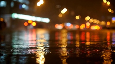 五颜六色的交通灯波克圆圈倒映在夜间城市街道上的水中，点缀着细小的雨滴。慢动作视频
