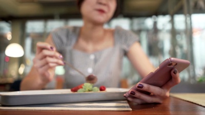笑容可掬的快乐亚洲女性喜欢在咖啡店吃巧克力蛋糕甜点，并在手机上享受在线购物的乐趣