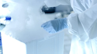 医学病毒学研究科学家穿着带有面罩的危险品西装，她用从冰箱盒子中分离出来的病毒串检查试管。她在一家无菌高科技实验室/研究机构工作。